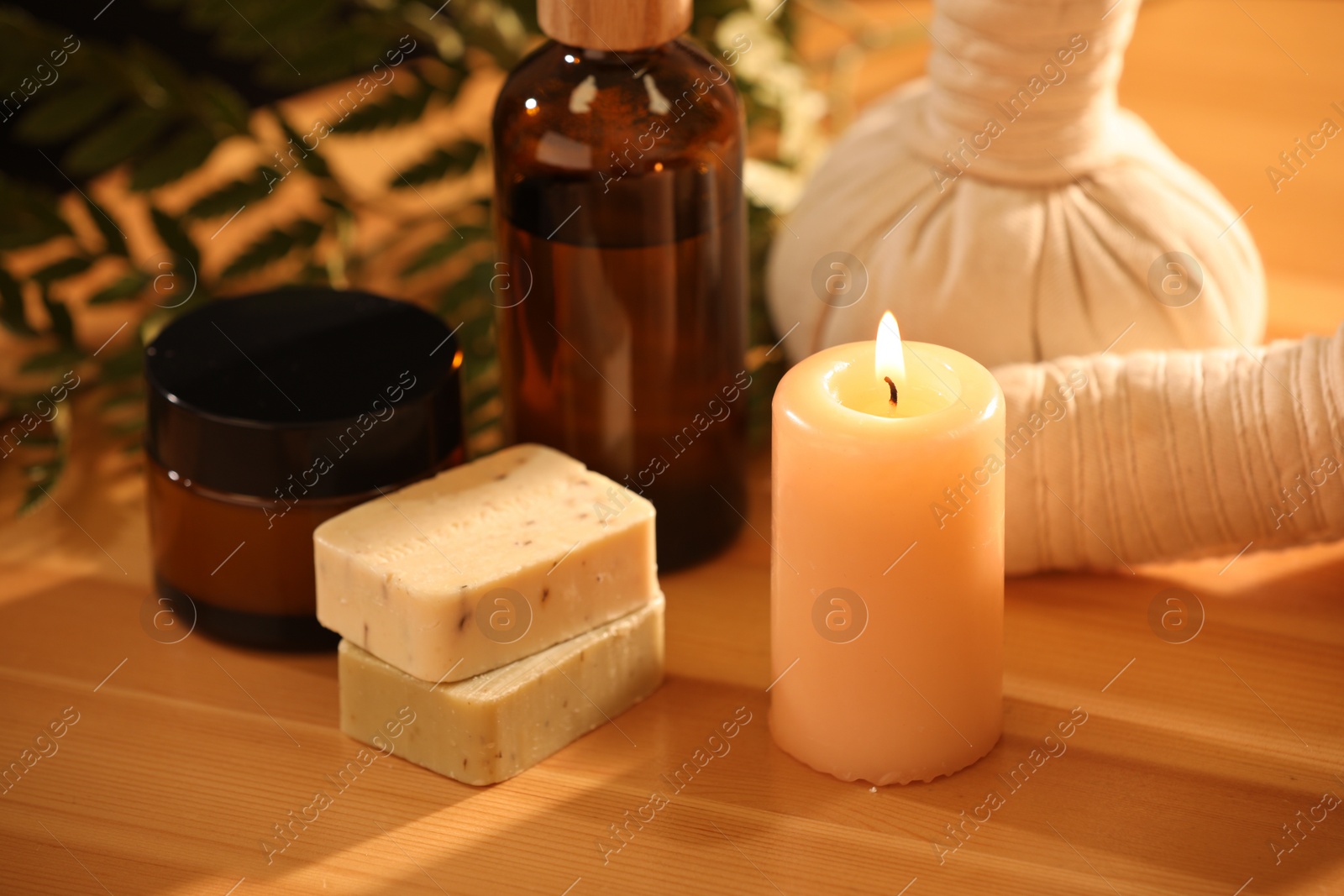 Photo of Spa composition. Cosmetic products, herbal bags and burning candle on wooden table, closeup