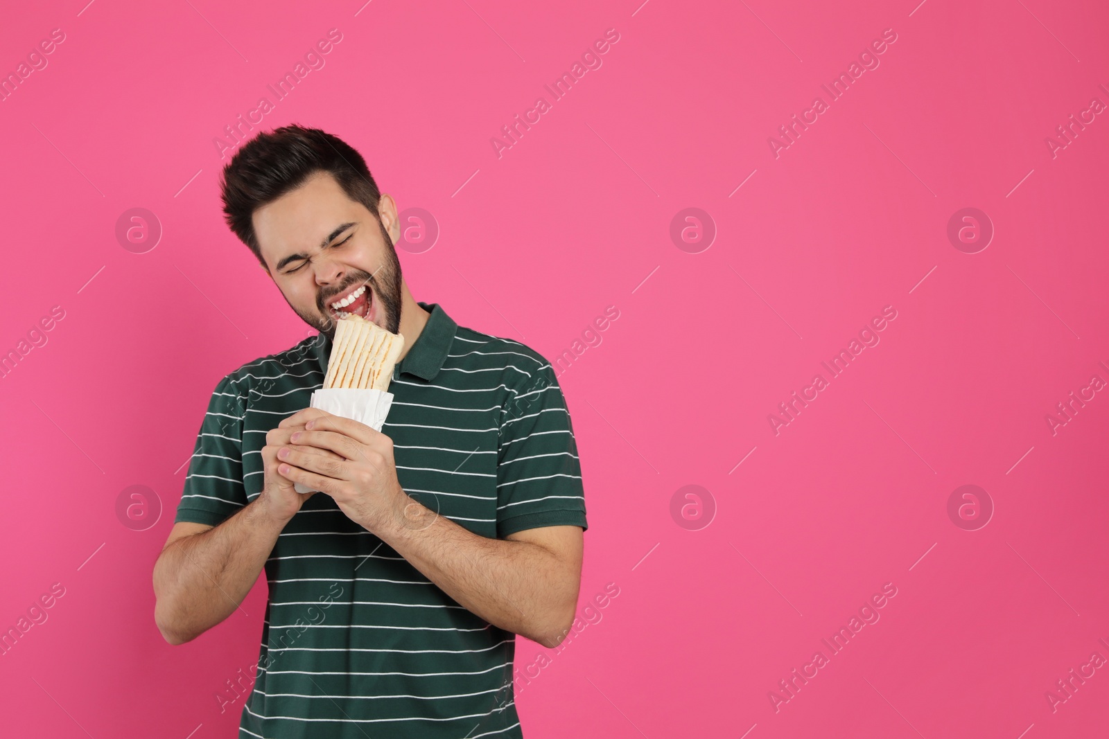 Photo of Young man eating tasty shawarma on pink background. Space for text