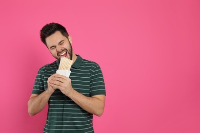 Young man eating tasty shawarma on pink background. Space for text