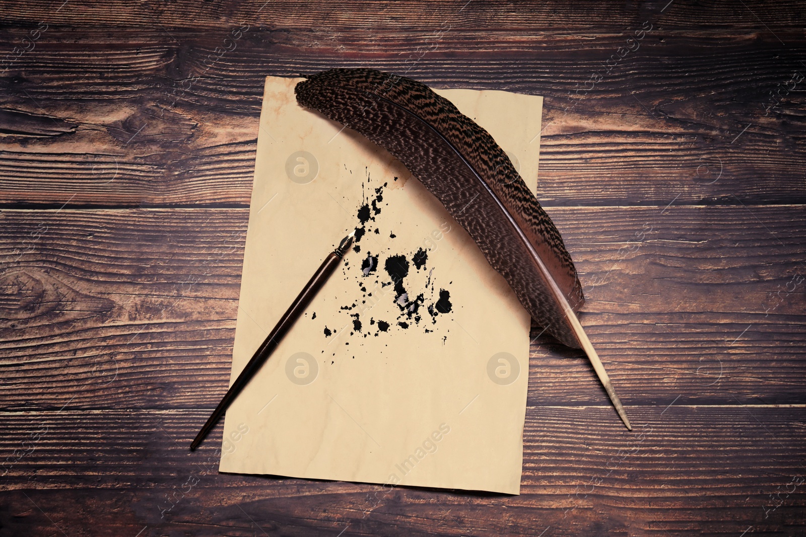 Photo of Feather, fountain pen and vintage parchment with ink stains on wooden table, top view