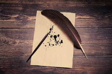 Feather, fountain pen and vintage parchment with ink stains on wooden table, top view