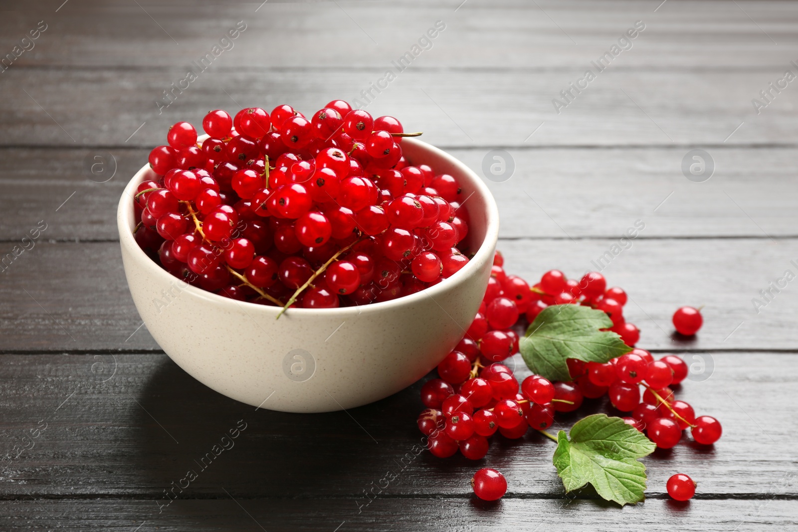 Photo of Delicious red currants and leaves on dark wooden table