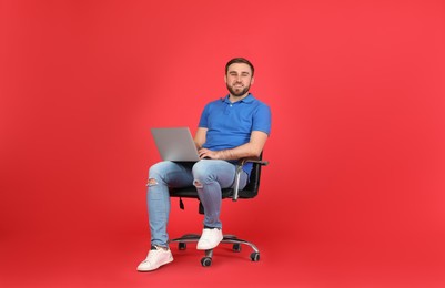 Photo of Young man with laptop sitting in comfortable office chair on red background