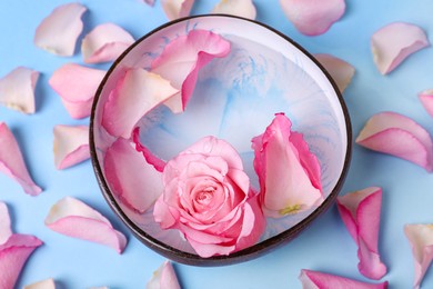 Photo of Bowl with water and rose petals on light blue background, above view. Spa composition