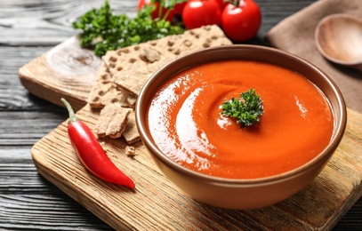 Photo of Bowl with fresh homemade tomato soup on wooden board