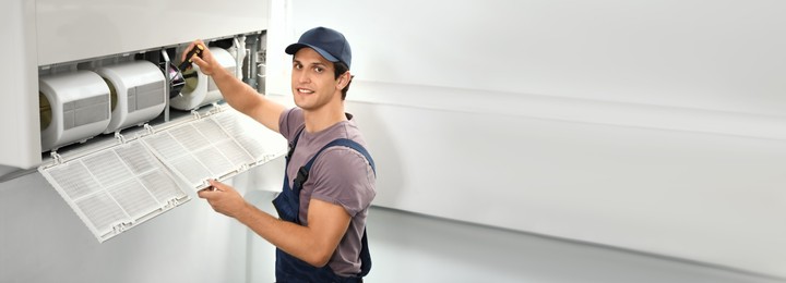 Male technician repairing air conditioner indoors, space for text. Banner design