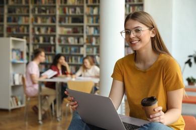 Photo of Young woman working on laptop in library. Space for text