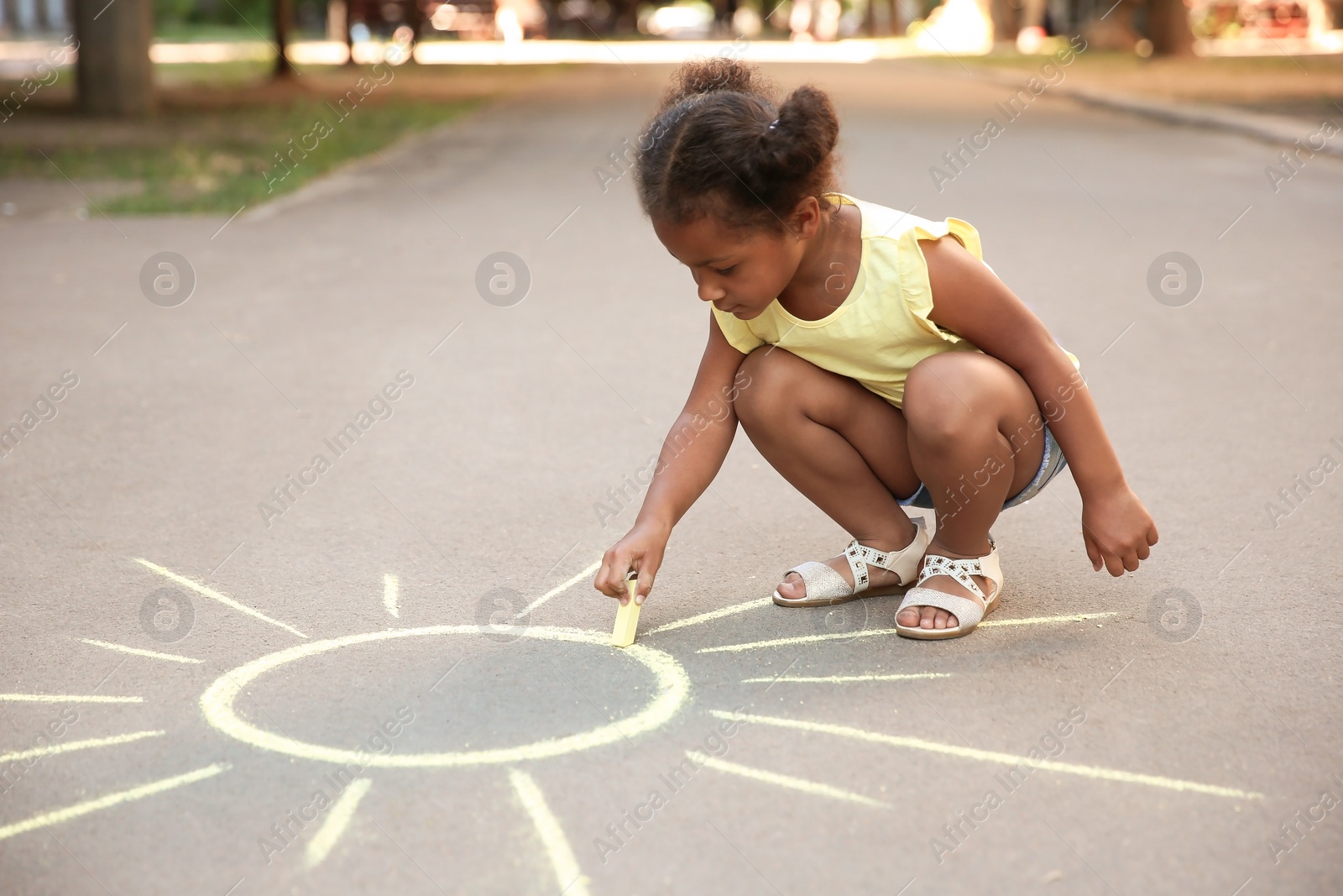 Photo of Little African-American child drawing sun with chalk on asphalt