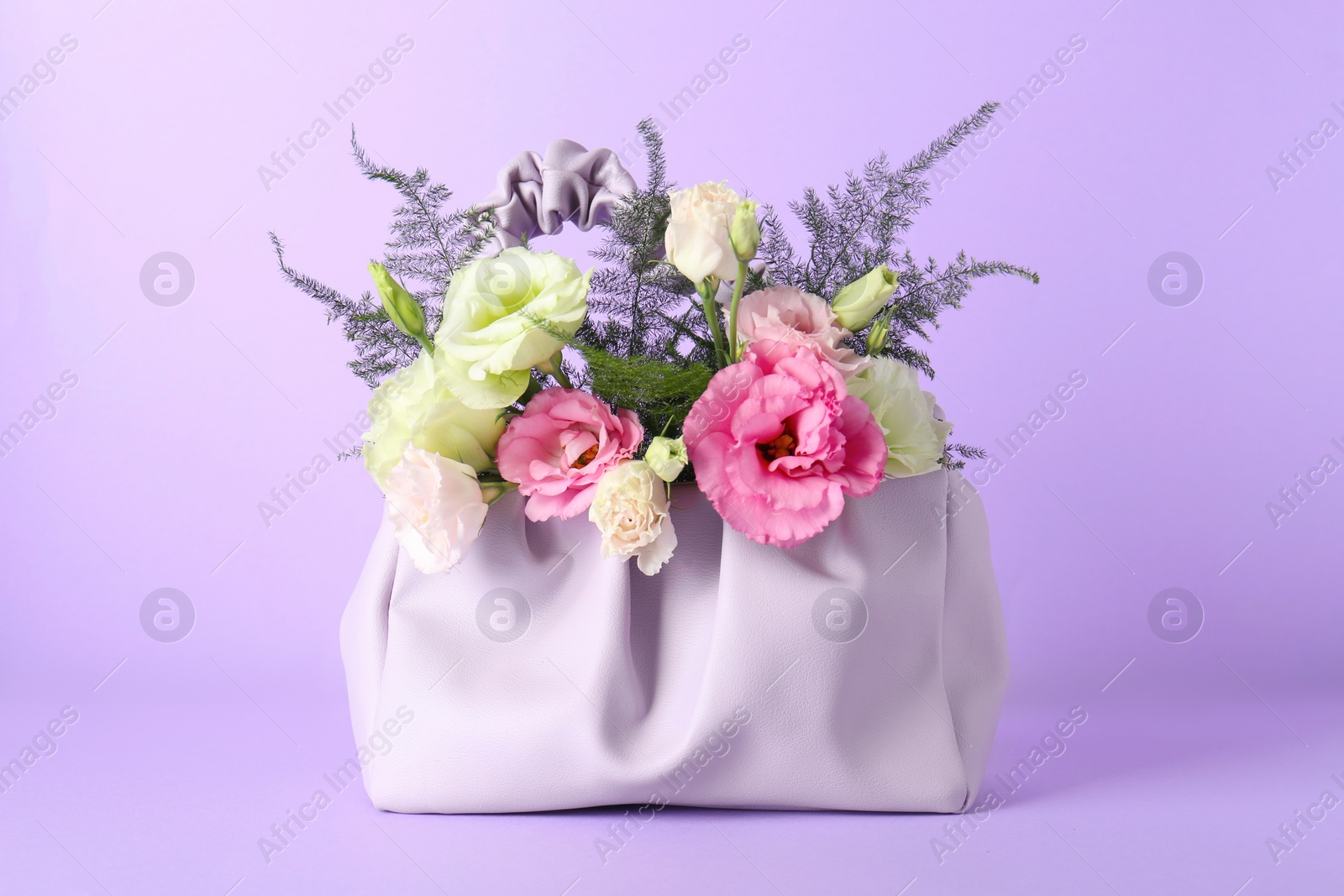 Photo of Stylish women's bag with beautiful flowers on violet background