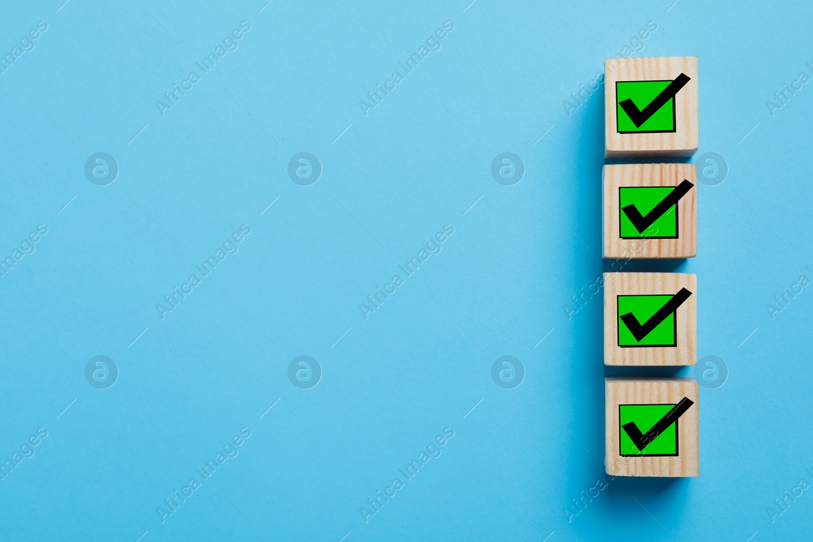 Image of Wooden cubes with check marks on light blue background, top view. Space for text