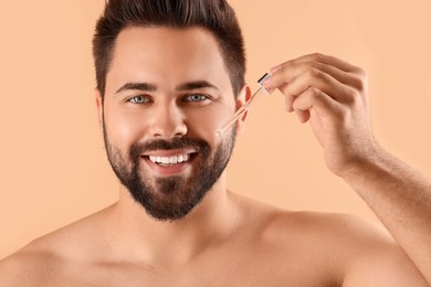 Handsome man applying cosmetic serum onto face on beige background