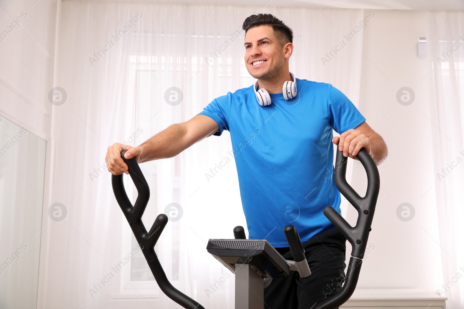 Photo of Man with headphones using modern elliptical machine at home