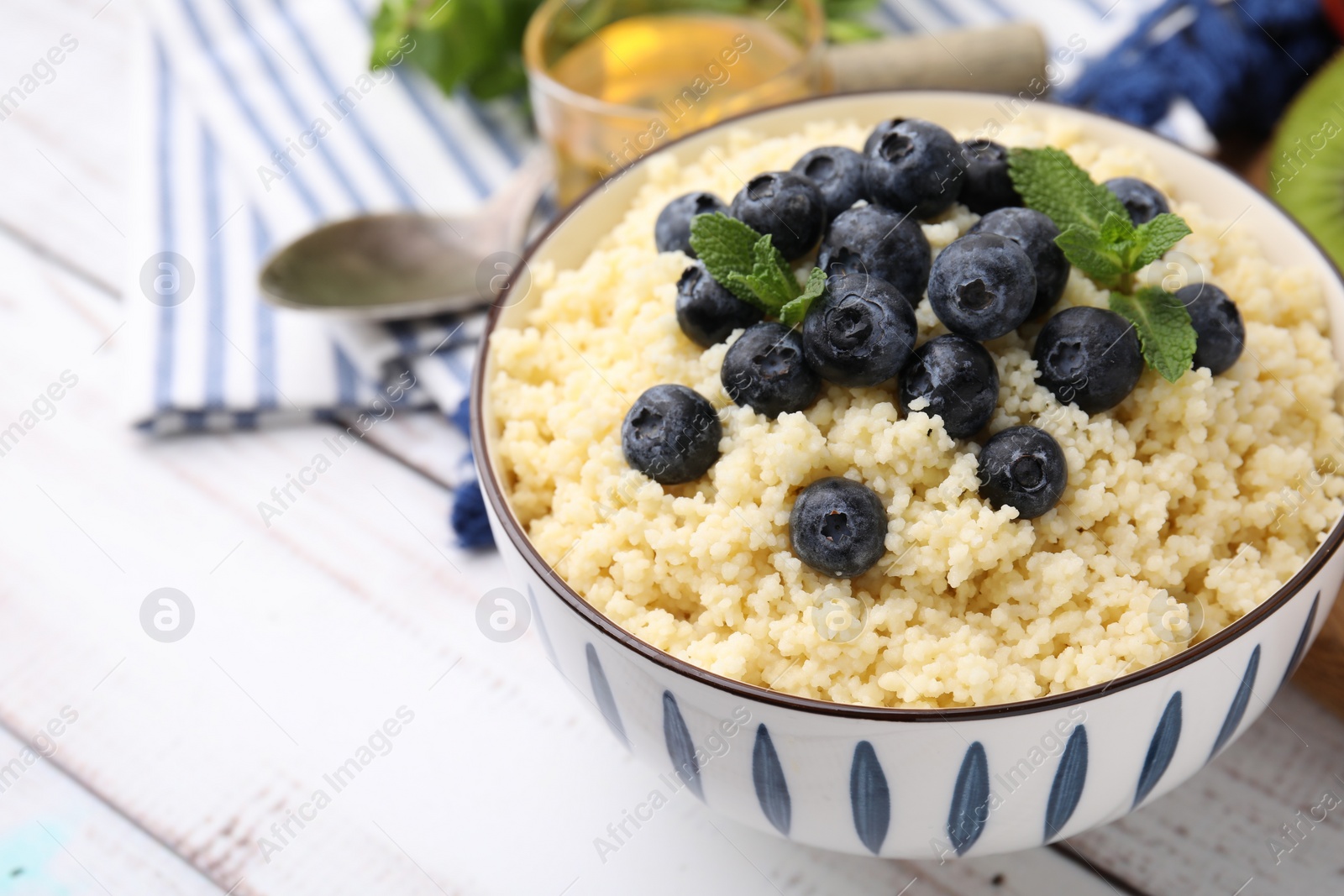 Photo of Bowl of tasty couscous with blueberries and mint on white table, closeup. Space for text