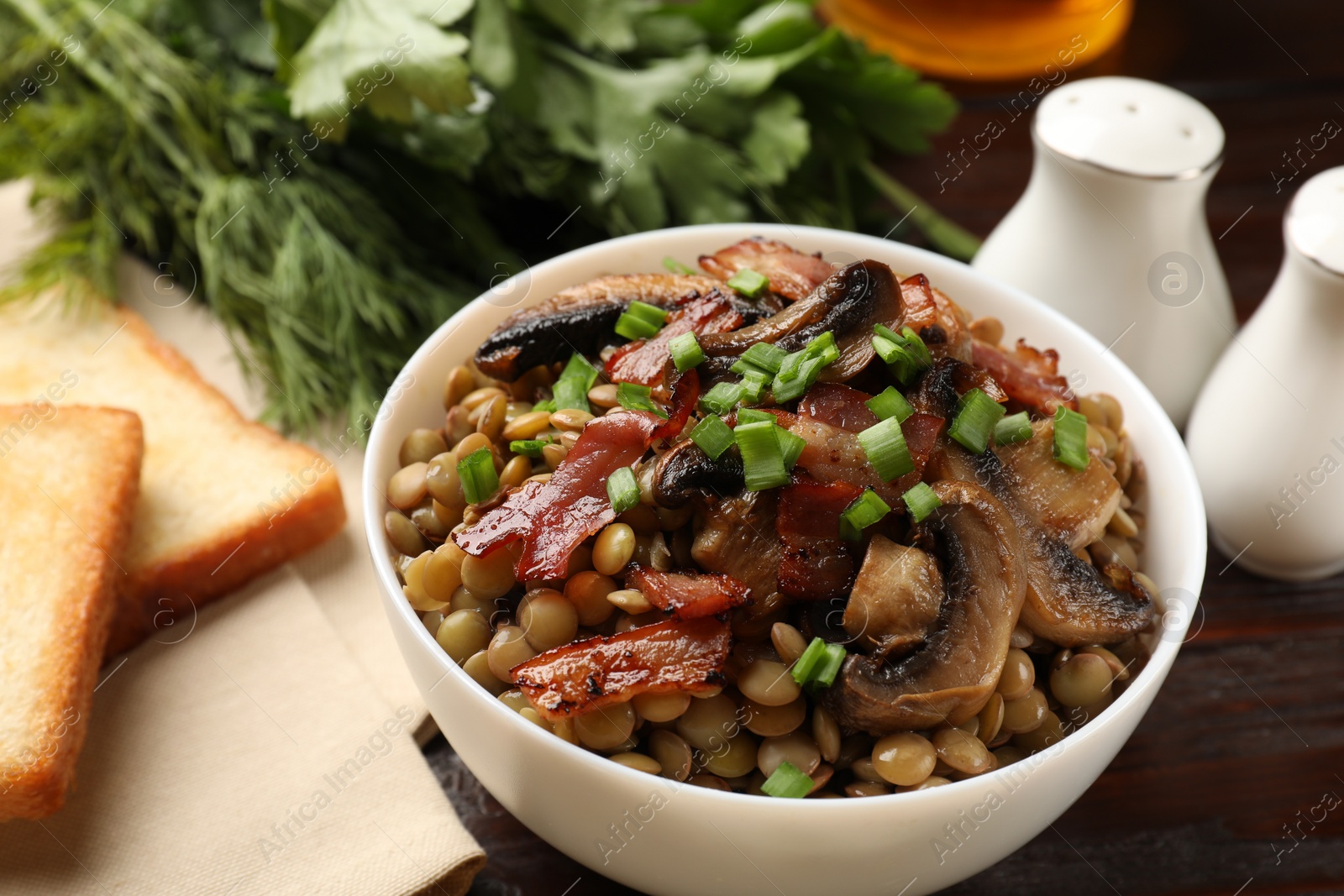 Photo of Delicious lentils with mushrooms, bacon and green onion in bowl served on table, closeup