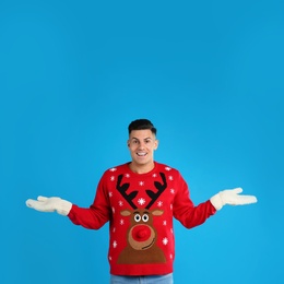 Photo of Happy man in Christmas sweater and mittens on blue background