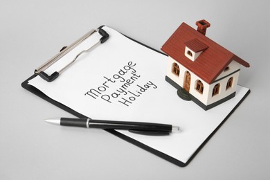 Photo of House model, clipboard with text Mortgage payment holiday and pen on light grey table