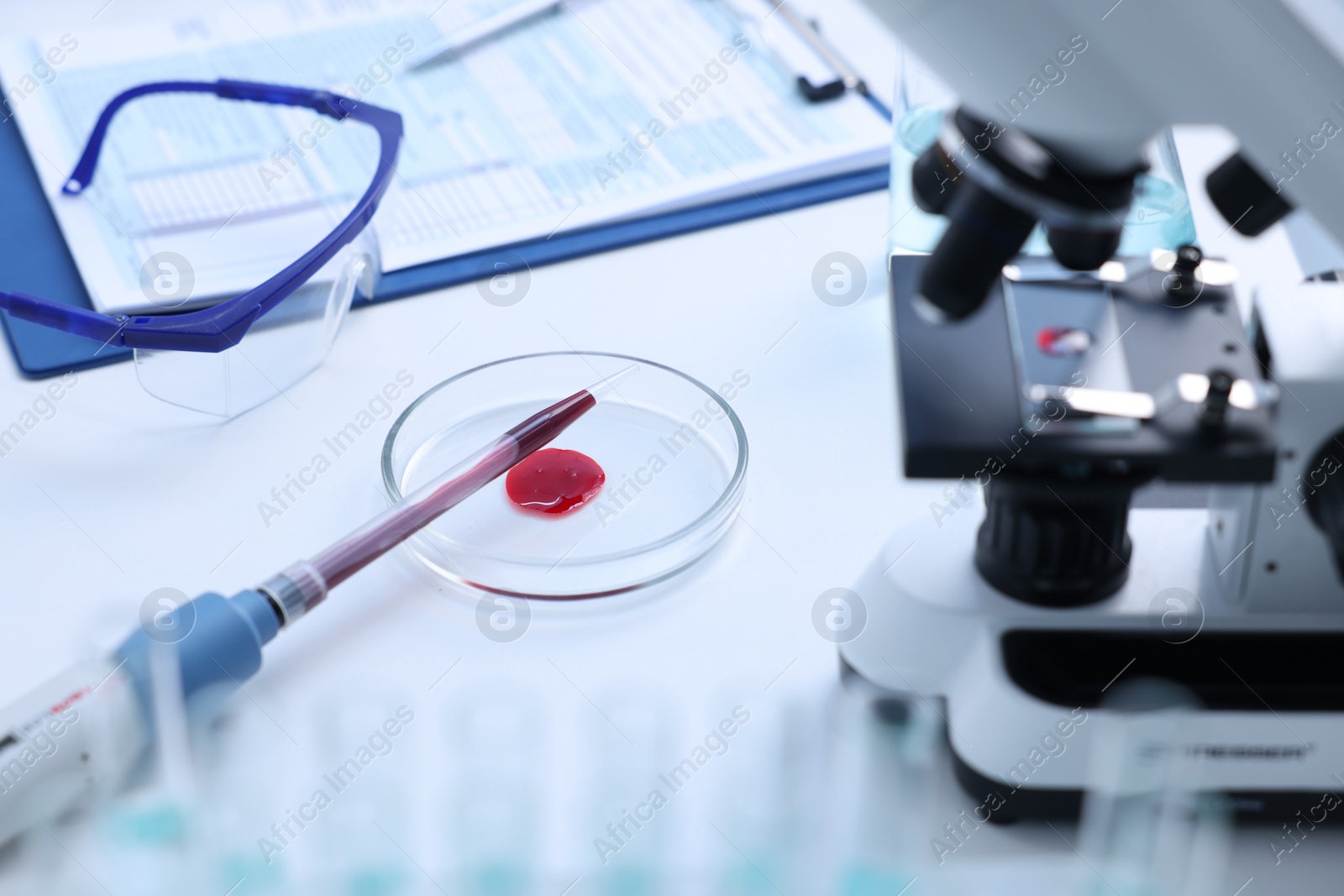 Photo of Modern medical microscope and Petri dish with blood sample on white table in laboratory, closeup