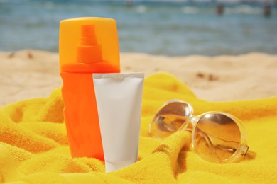 Photo of Sunscreen, sunglasses and towel on sandy beach. Sun protection care