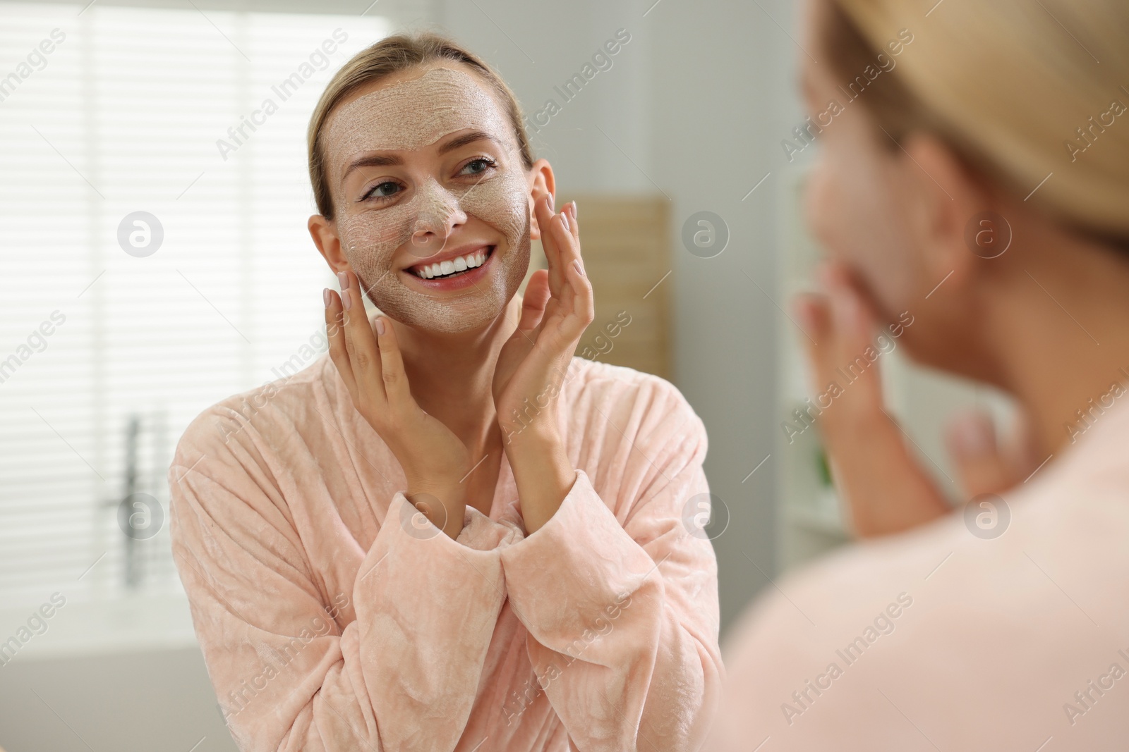 Photo of Woman applying face mask near mirror in bathroom. Spa treatments