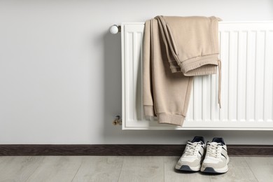 Photo of Heating radiator with beige pants and sneakers indoors. Space for text