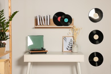 Photo of Table and stylish turntable near white wall decorated with vinyl records