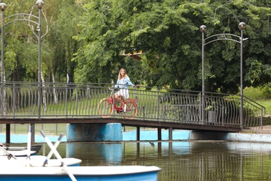 Photo of Beautiful woman in casual outfit with bicycle on bridge over pond