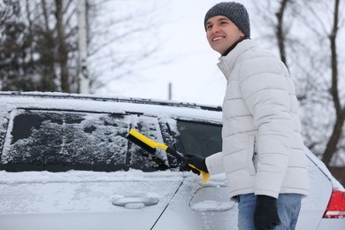 Photo of Man cleaning snow from car with brush outdoors, low angle view