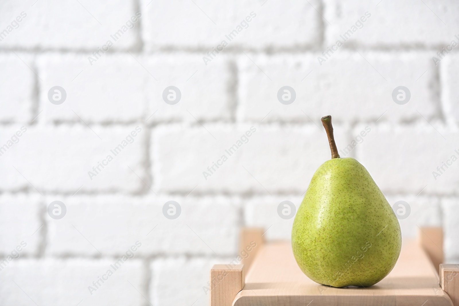 Photo of Ripe pear on wooden shelf against blurred background. Space for text