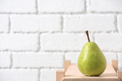 Ripe pear on wooden shelf against blurred background. Space for text