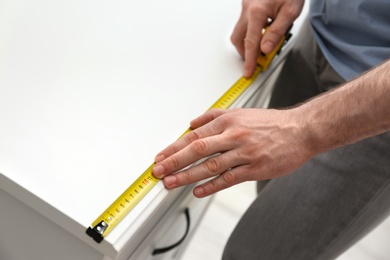 Man measuring chest of drawers indoors, closeup. Construction tool