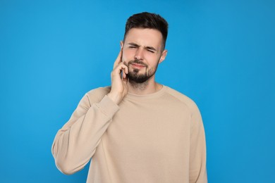 Young man suffering from ear pain on light blue background