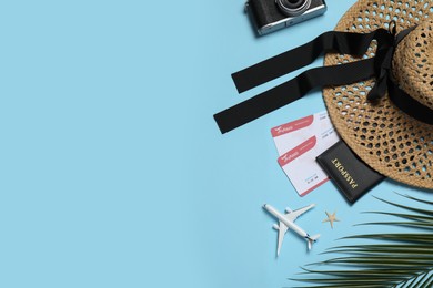 Photo of Passport with tickets, hat, camera, airplane model and palm leaf on light blue background, flat lay. Space for text