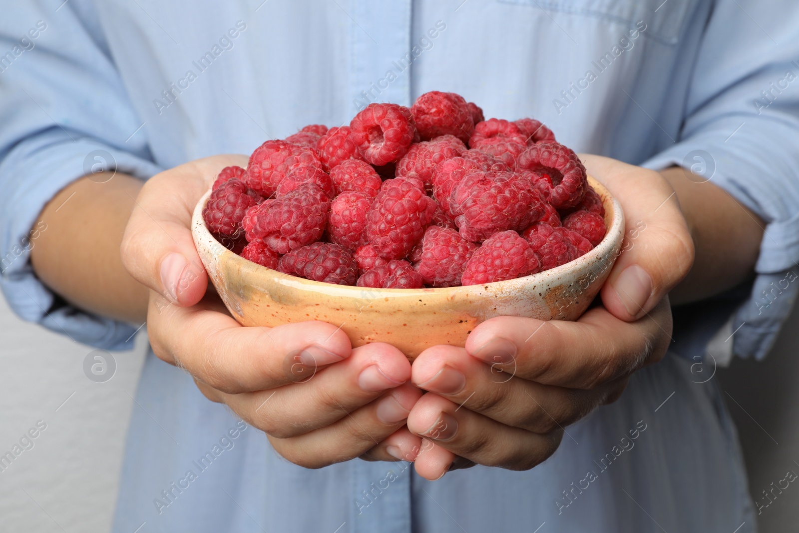 Photo of Woman holding bowl with delicious ripe raspberries, closeup