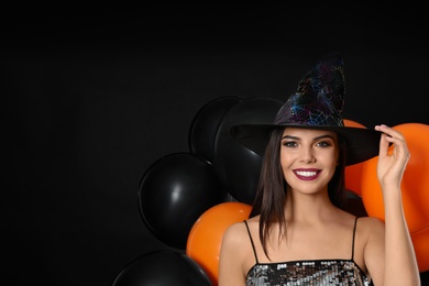 Photo of Beautiful woman wearing witch costume with balloons for Halloween party on black background, space for text