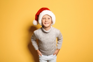 Photo of Cute little boy in warm sweater and Christmas hat on color background