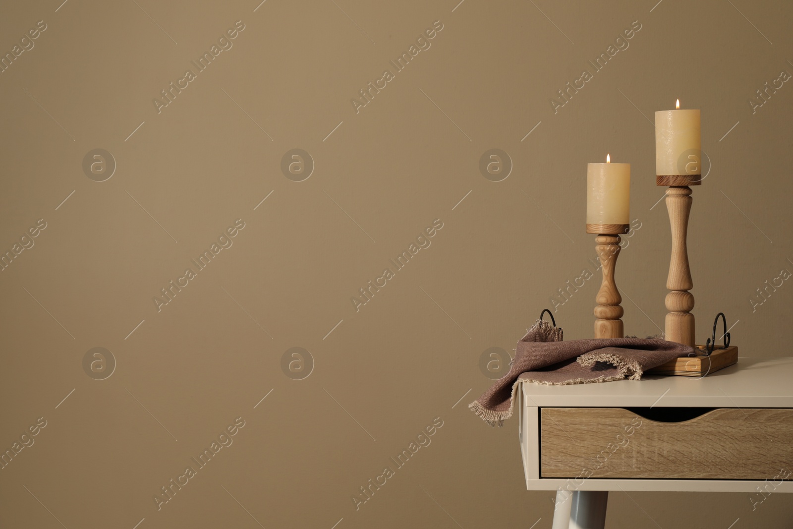 Photo of Holders with burning candles on white table near brown wall, space for text