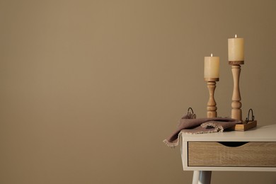 Holders with burning candles on white table near brown wall, space for text