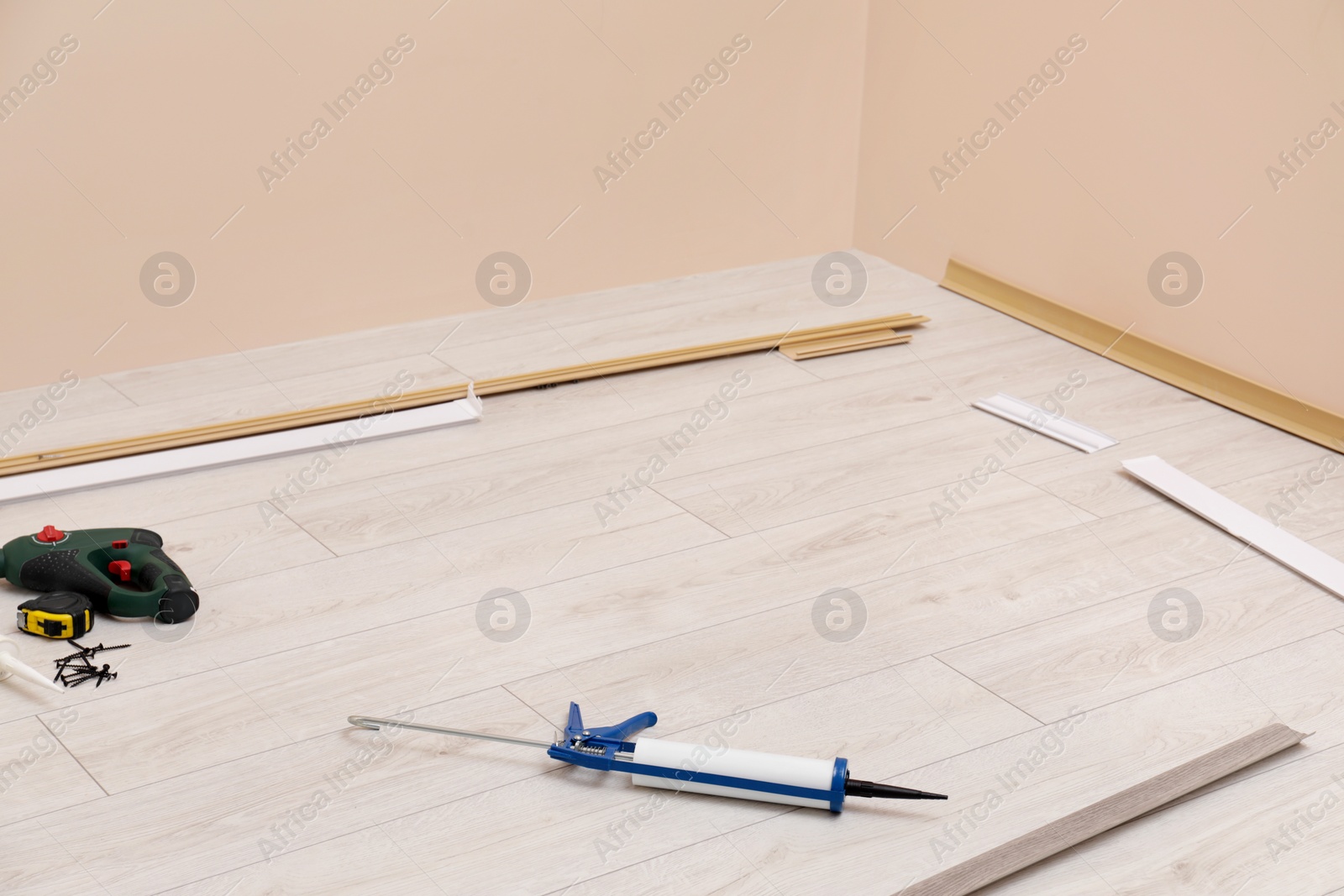 Photo of Plinths, caulking gun, screwdriver, measuring tape and screws on laminated floor in room