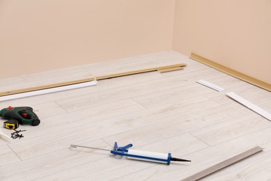 Photo of Plinths, caulking gun, screwdriver, measuring tape and screws on laminated floor in room