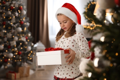 Cute little girl holding gift box in room decorated for Christmas