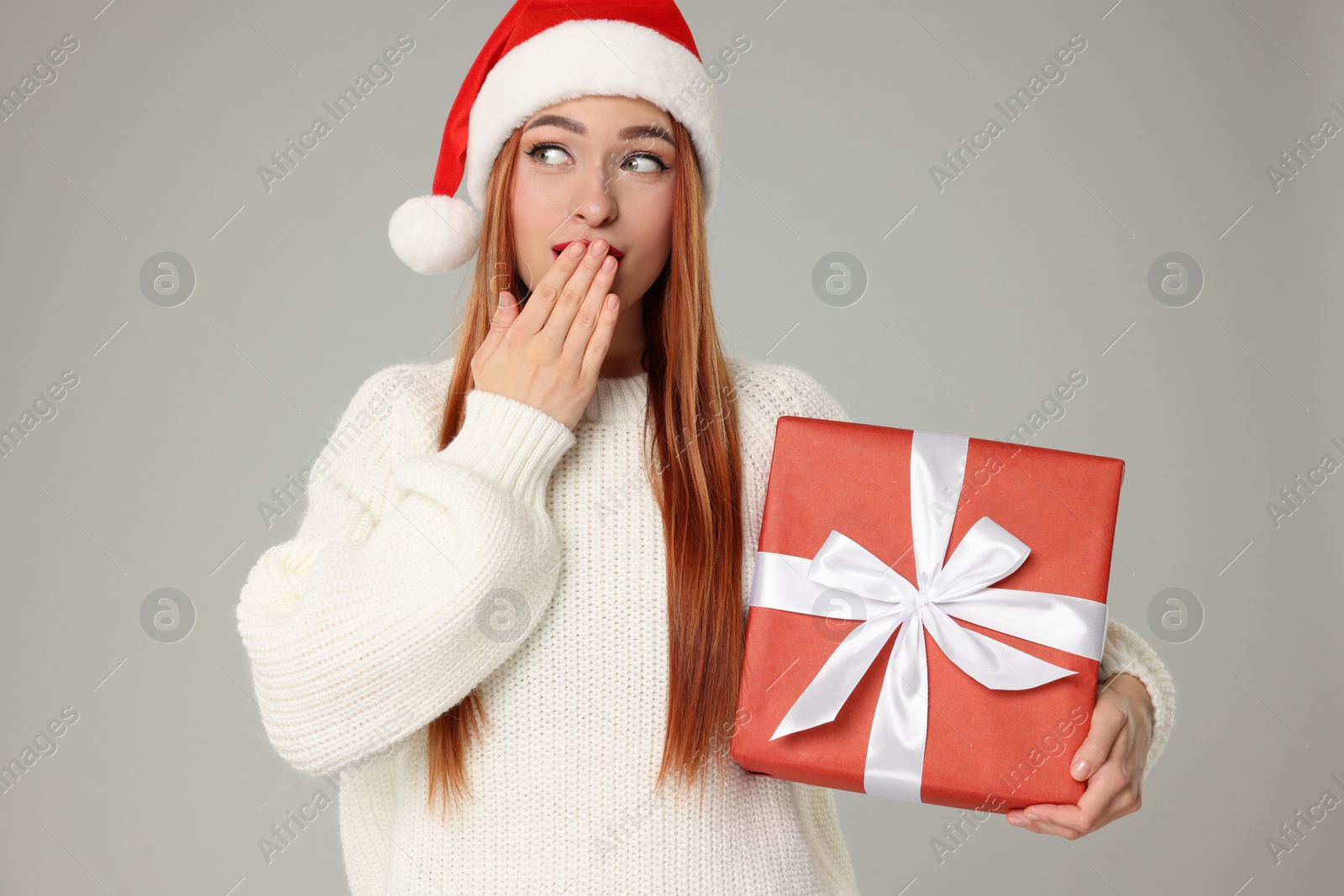 Photo of Emotional young woman in Santa hat with Christmas gift on light grey background