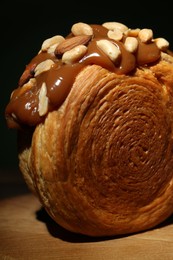 Photo of Round croissant with chocolate paste and nuts on wooden table, closeup. Tasty puff pastry