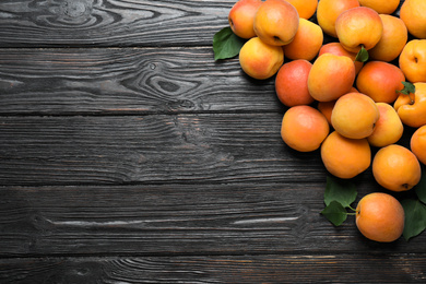 Many fresh ripe apricots on black wooden table, flat lay. Space for text