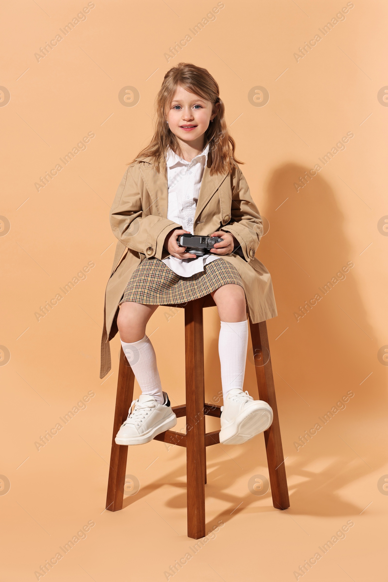 Photo of Fashion concept. Stylish girl with vintage camera on pale orange background