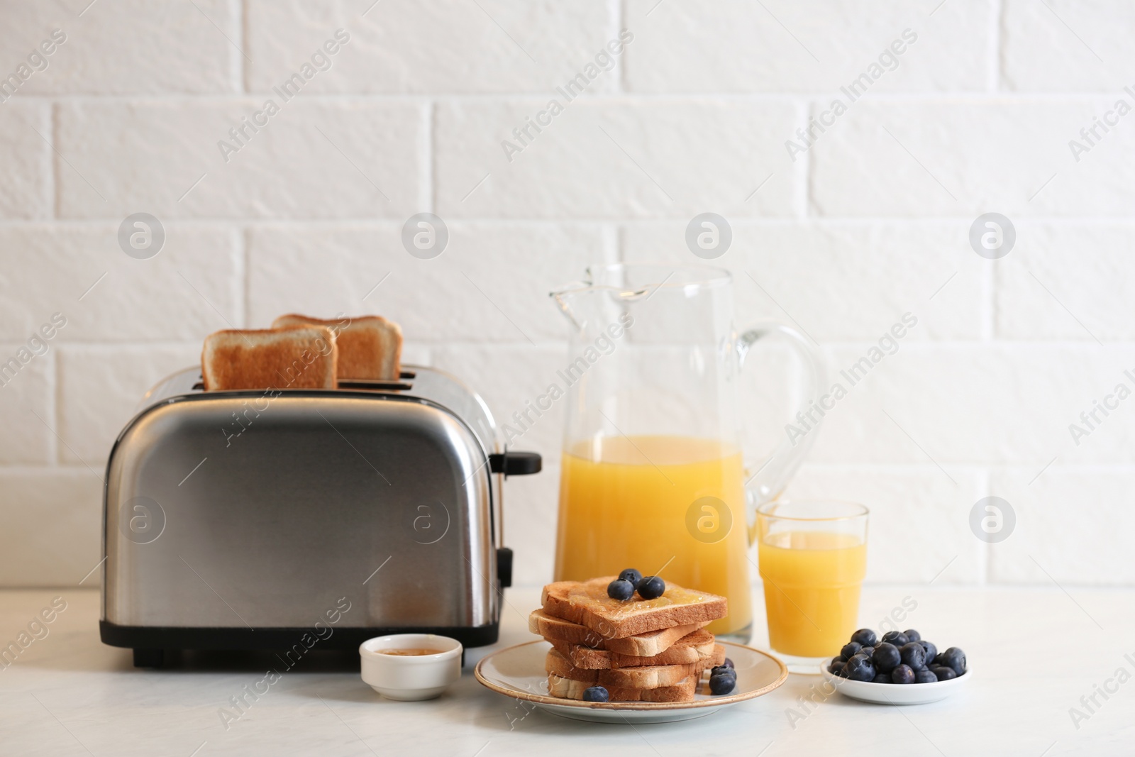 Photo of Modern toaster and tasty breakfast on white table near brick wall