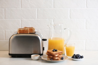 Modern toaster and tasty breakfast on white table near brick wall