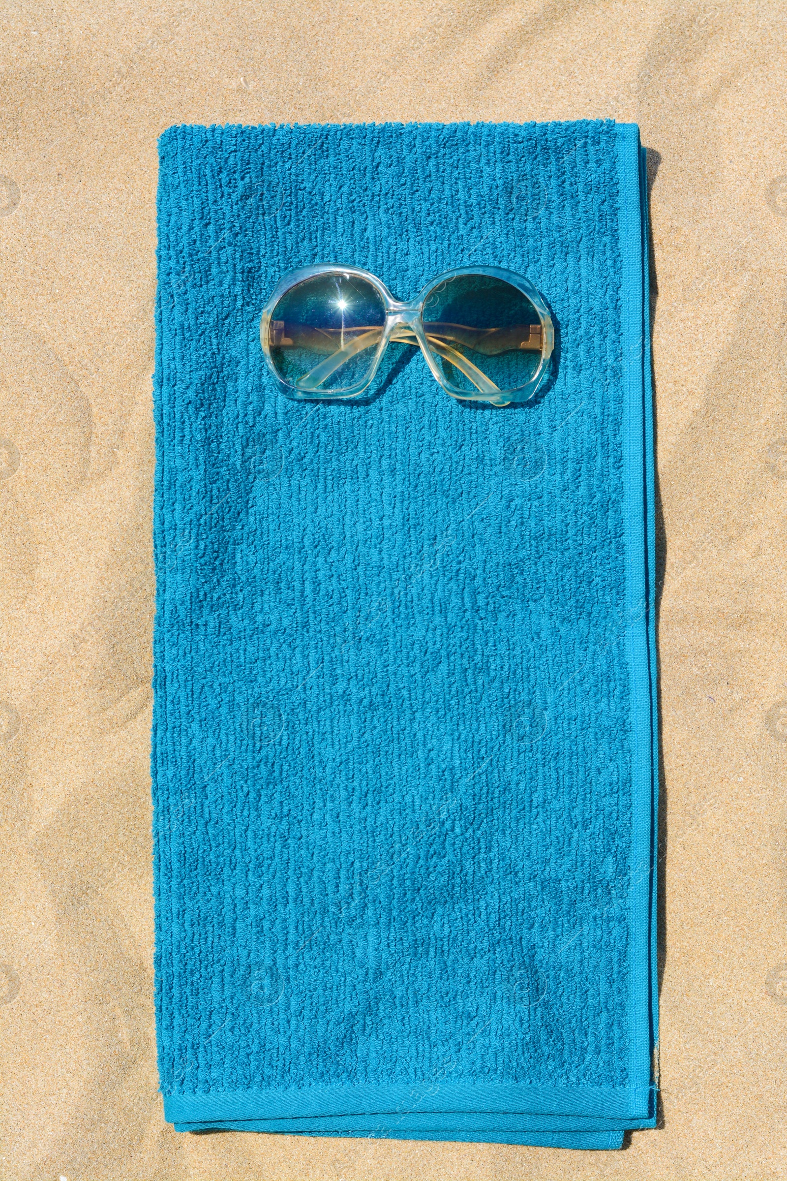 Photo of Soft blue beach towel with sunglasses on sand, top view