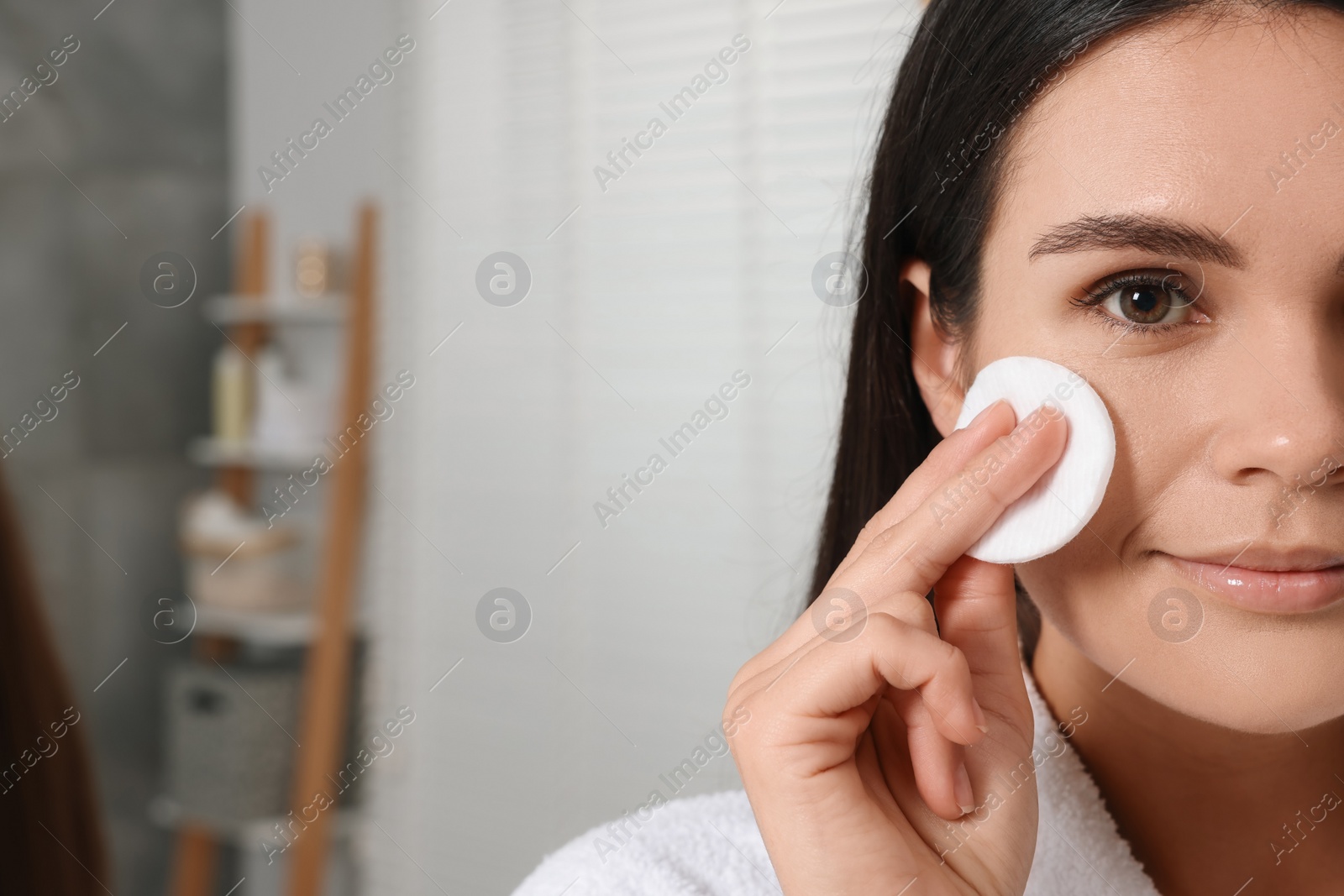 Photo of Young woman cleaning her face with cotton pad indoors, closeup. Space for text