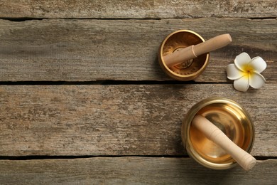 Photo of Golden singing bowls, mallets and flower on wooden table, flat lay. Space for text