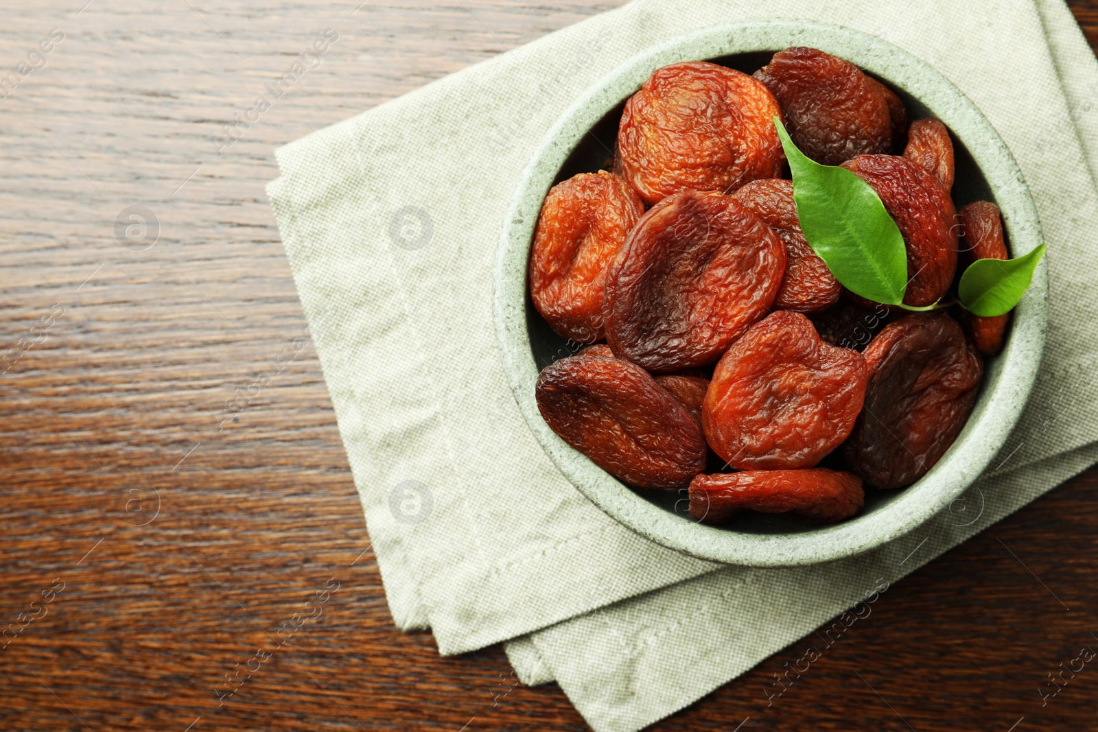 Photo of Tasty apricots in bowl on wooden table, top view and space for text. Dried fruits